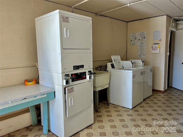 community laundry room featuring stacked washer and clothes dryer, concrete block wall, and a sink