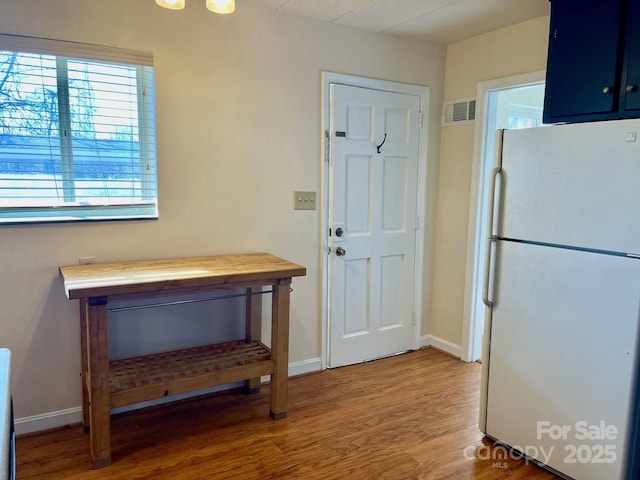 interior space featuring visible vents, baseboards, light wood-type flooring, freestanding refrigerator, and blue cabinets