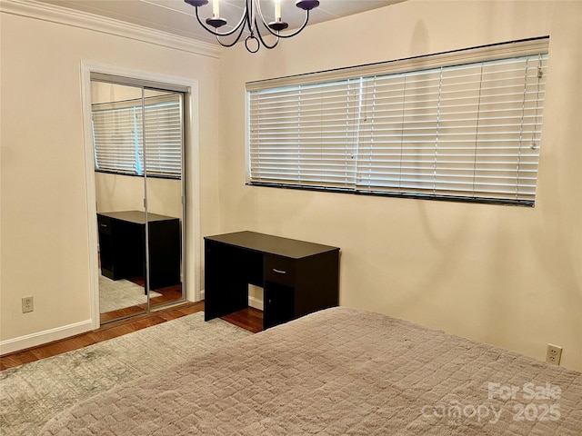 unfurnished bedroom featuring wood finished floors, baseboards, an inviting chandelier, ornamental molding, and a closet