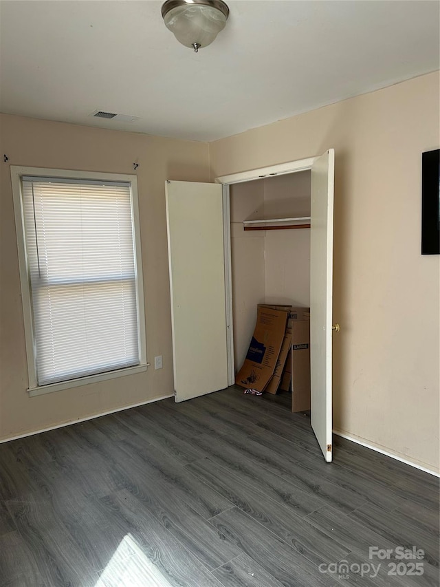 unfurnished bedroom with dark wood-type flooring, visible vents, and a closet