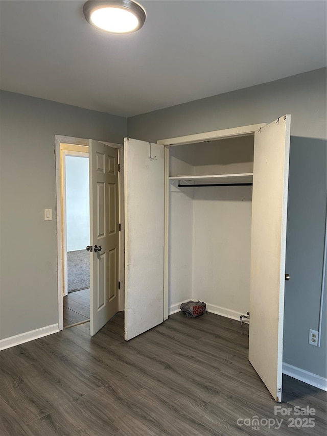 unfurnished bedroom with dark wood-style floors, baseboards, and a closet