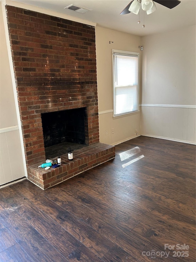 unfurnished living room with a wainscoted wall, a brick fireplace, visible vents, and wood finished floors