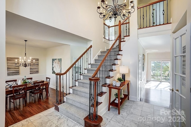 stairway featuring baseboards, a high ceiling, marble finish floor, and a chandelier