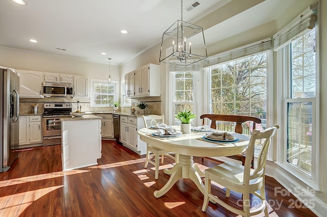 dining area with a wealth of natural light, visible vents, dark wood finished floors, and crown molding