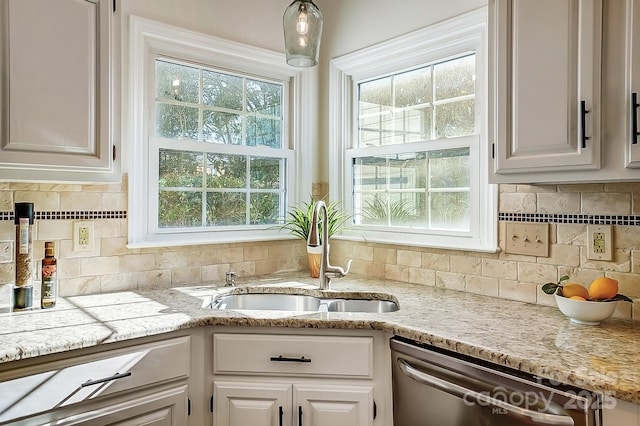 kitchen with backsplash, light stone countertops, dishwasher, white cabinets, and a sink