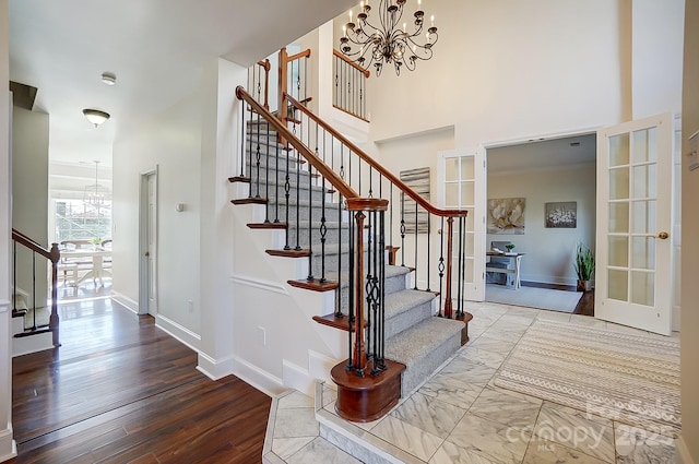 stairs featuring a notable chandelier, a high ceiling, baseboards, and wood finished floors