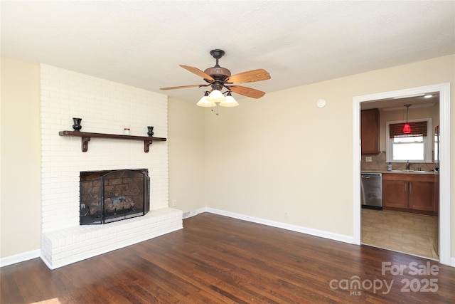 unfurnished living room featuring dark wood finished floors, a fireplace, baseboards, and a sink