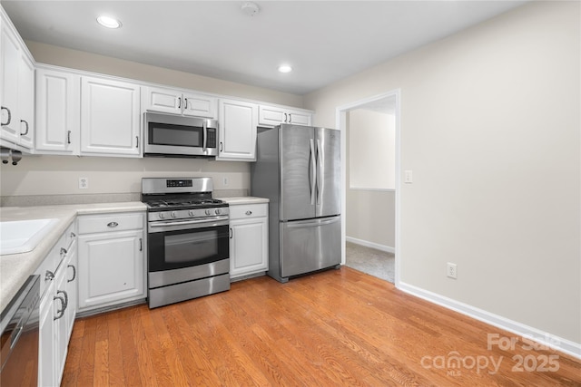 kitchen featuring light wood finished floors, white cabinetry, stainless steel appliances, and light countertops