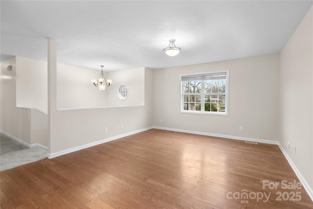 unfurnished room with a notable chandelier, baseboards, and wood finished floors