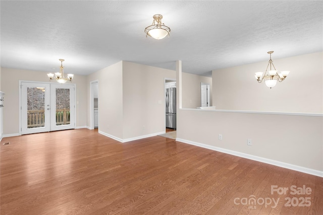 unfurnished living room featuring baseboards, french doors, an inviting chandelier, wood finished floors, and a textured ceiling