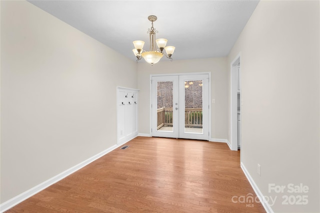 interior space featuring light wood finished floors, a notable chandelier, french doors, and baseboards