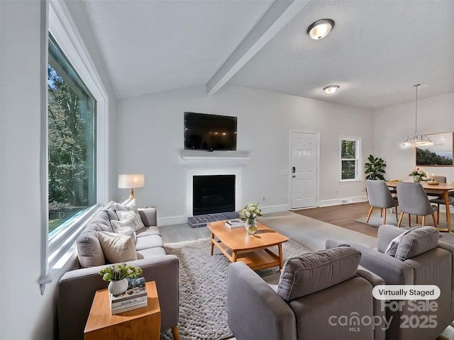 living room featuring wood finished floors, vaulted ceiling with beams, a fireplace with raised hearth, and baseboards