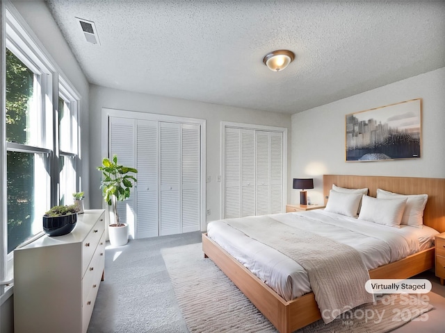 carpeted bedroom with visible vents, two closets, and a textured ceiling