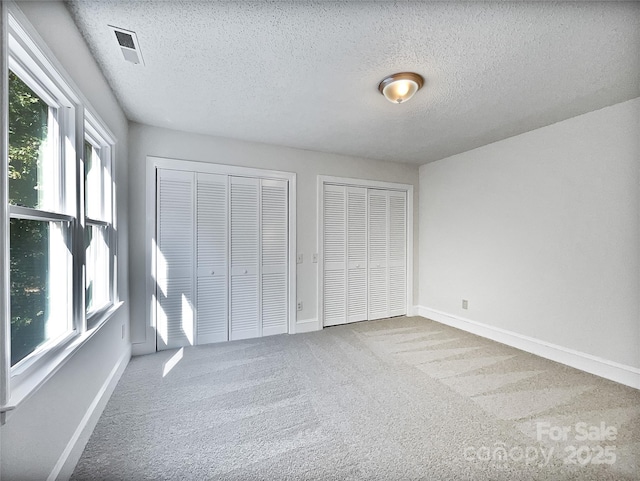 unfurnished bedroom with visible vents, baseboards, multiple closets, carpet flooring, and a textured ceiling