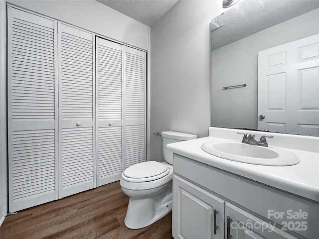 bathroom with vanity, wood finished floors, a closet, a textured ceiling, and toilet