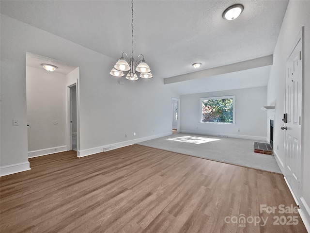 unfurnished living room featuring visible vents, a fireplace with raised hearth, baseboards, wood finished floors, and a notable chandelier