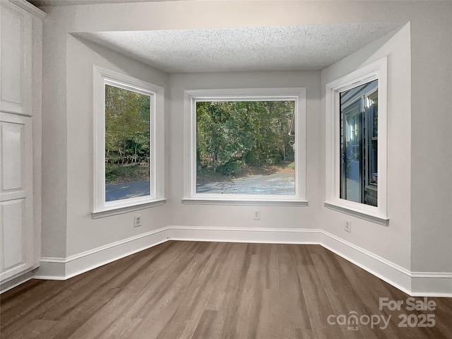 empty room with a textured ceiling, dark wood-type flooring, and baseboards