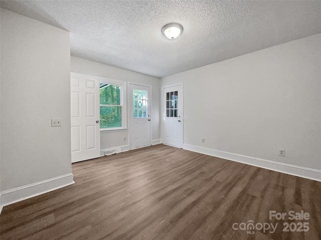 spare room featuring dark wood finished floors, a textured ceiling, and baseboards