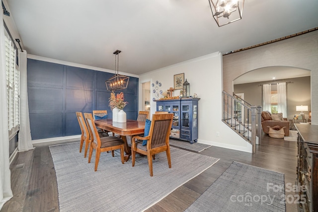 dining area with stairway, dark wood-style floors, arched walkways, ornamental molding, and a chandelier