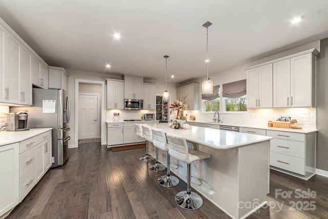 kitchen featuring a sink, a kitchen breakfast bar, dark wood-style floors, a center island, and stainless steel appliances