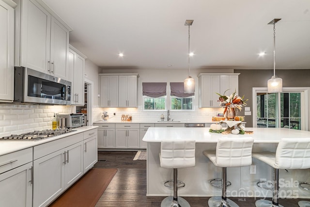 kitchen featuring a kitchen bar, a sink, dark wood finished floors, stainless steel appliances, and light countertops