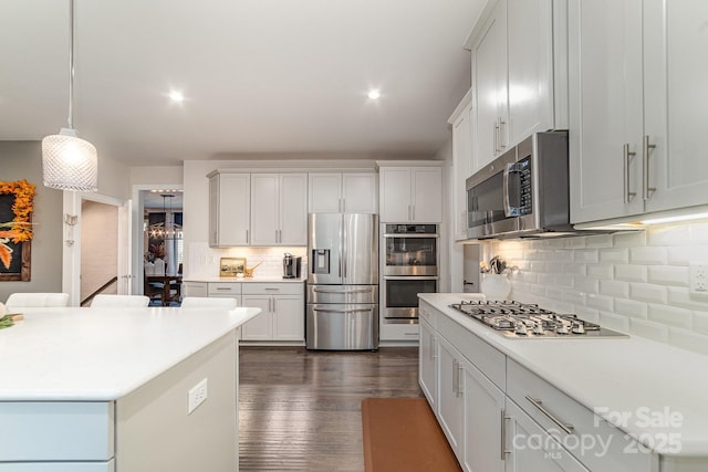 kitchen with pendant lighting, tasteful backsplash, dark wood finished floors, appliances with stainless steel finishes, and light countertops