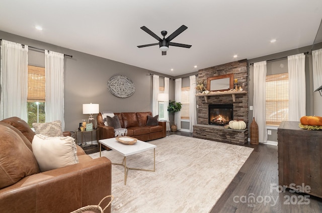 living area with a wealth of natural light, a ceiling fan, dark wood-type flooring, and a fireplace