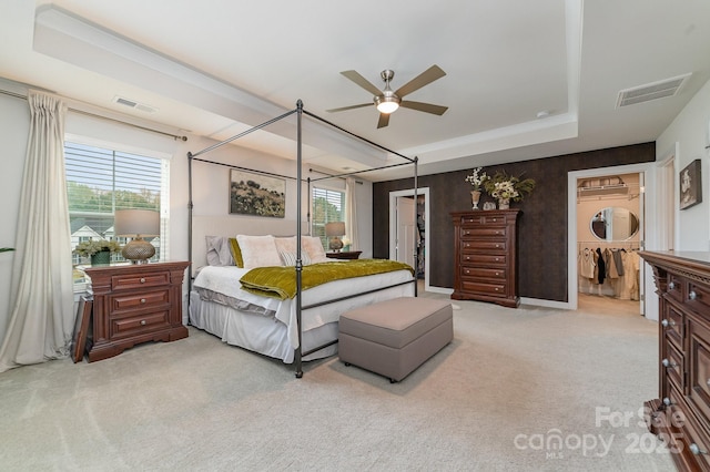 bedroom with a tray ceiling, multiple windows, light colored carpet, and visible vents