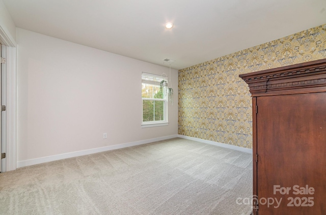 empty room featuring baseboards, visible vents, wallpapered walls, and carpet