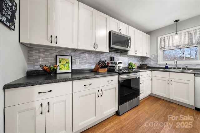 kitchen with light wood finished floors, decorative backsplash, stainless steel appliances, and a sink