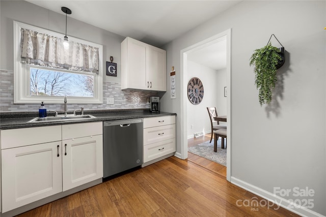 kitchen with light wood-style flooring, a sink, tasteful backsplash, dark countertops, and dishwasher