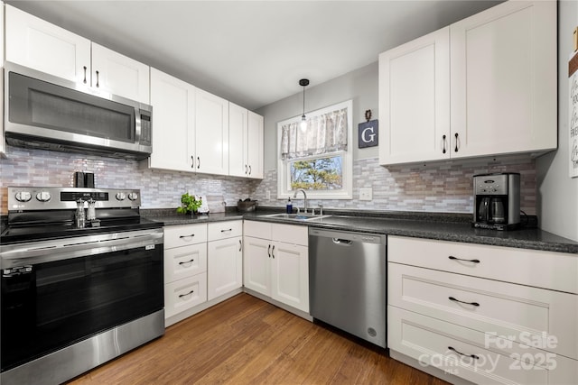 kitchen featuring dark countertops, light wood-type flooring, stainless steel appliances, white cabinetry, and a sink