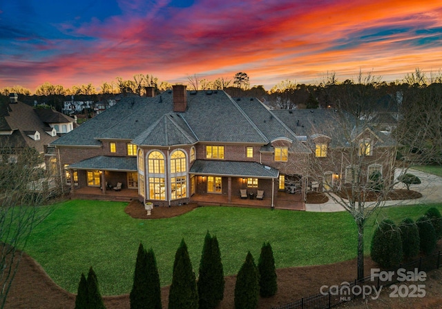 back of property at dusk with a yard, a patio area, driveway, and a chimney