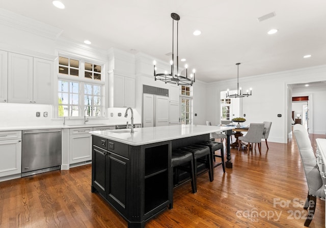 kitchen featuring a kitchen island with sink, a sink, white cabinets, stainless steel dishwasher, and dark cabinets