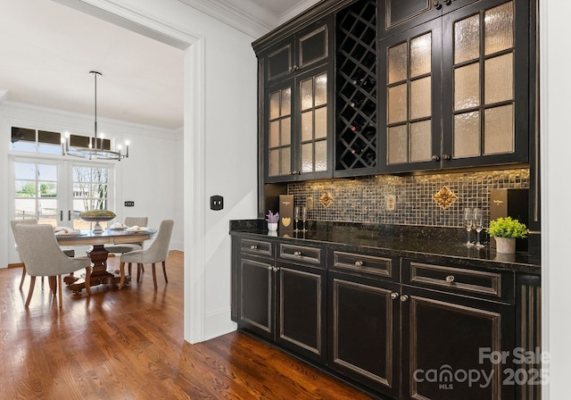 bar with backsplash, crown molding, dark wood-type flooring, a dry bar, and a notable chandelier