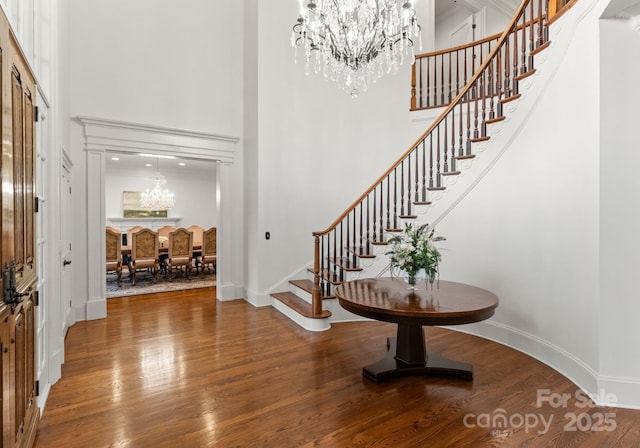 entryway featuring wood finished floors, baseboards, an inviting chandelier, a high ceiling, and stairs