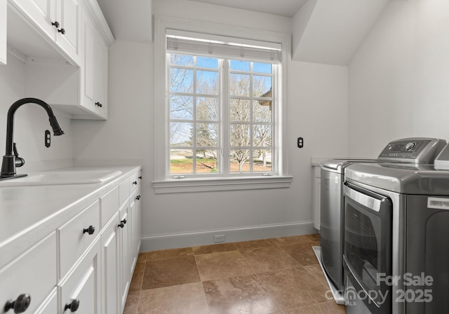 washroom with a sink, baseboards, cabinet space, and washing machine and clothes dryer