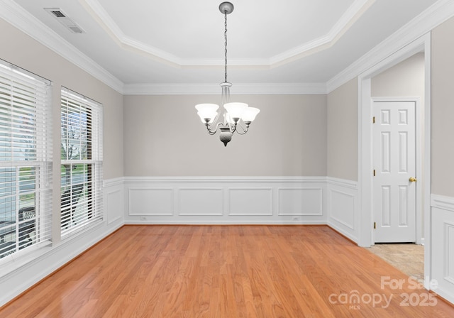 spare room featuring visible vents, light wood-style flooring, wainscoting, a raised ceiling, and a chandelier