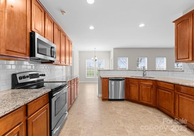 kitchen with light stone counters, a sink, appliances with stainless steel finishes, brown cabinets, and backsplash