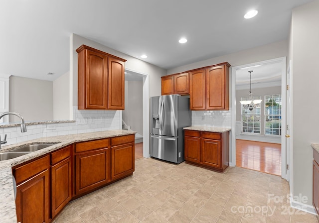 kitchen featuring tasteful backsplash, stainless steel fridge with ice dispenser, light stone counters, brown cabinets, and a sink