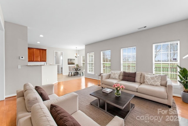 living room with visible vents, baseboards, recessed lighting, light wood-style floors, and a notable chandelier