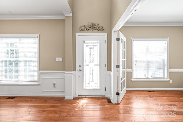 entrance foyer with visible vents, a wainscoted wall, ornamental molding, and light wood finished floors