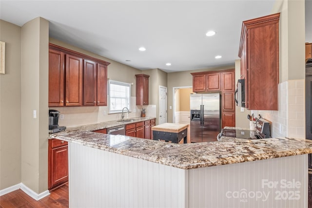 kitchen with tasteful backsplash, dark wood finished floors, a peninsula, stainless steel appliances, and a sink