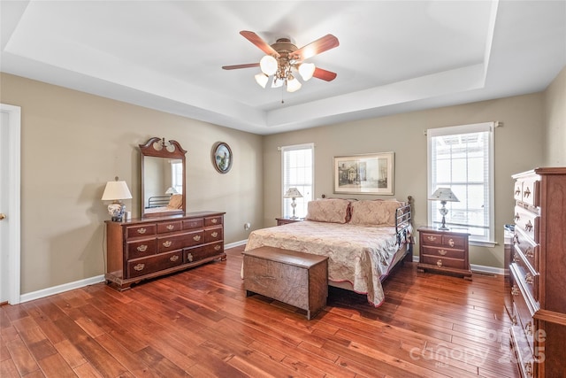 bedroom with a ceiling fan, a raised ceiling, baseboards, and hardwood / wood-style floors