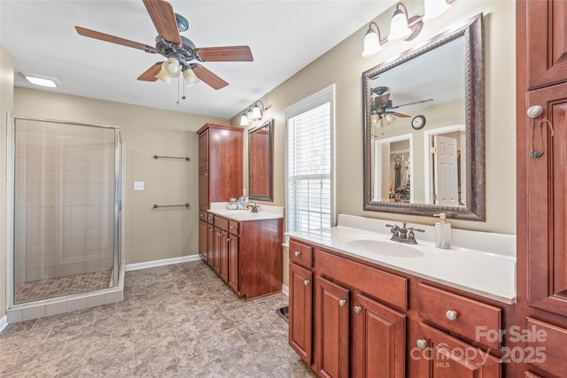 bathroom with a shower stall, baseboards, two vanities, a ceiling fan, and a sink