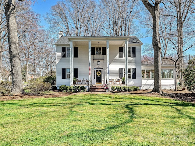 greek revival inspired property with covered porch, a chimney, and a front lawn