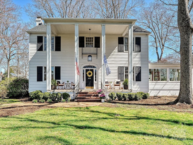 view of front of house featuring a chimney, covered porch, and a front yard