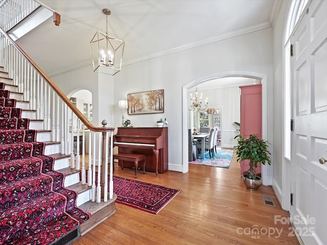 entryway with visible vents, arched walkways, a notable chandelier, and hardwood / wood-style flooring