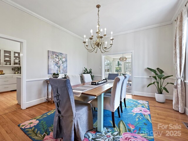 dining room with baseboards, a chandelier, crown molding, and light wood finished floors