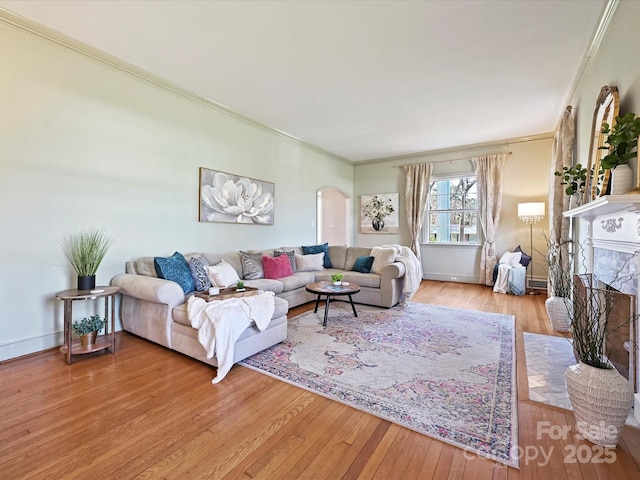 living room with light wood finished floors, a brick fireplace, crown molding, baseboards, and arched walkways